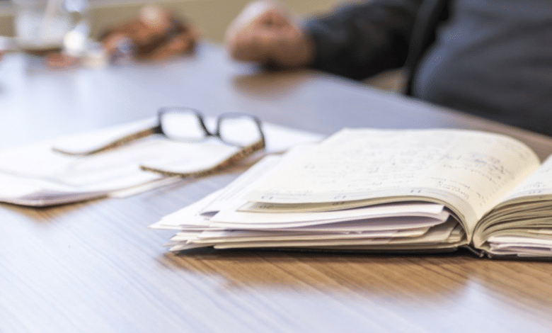 Imagen que muestra un cuaderno co apuntes, unos lentes de aumento y personas durante su descanso laboral
